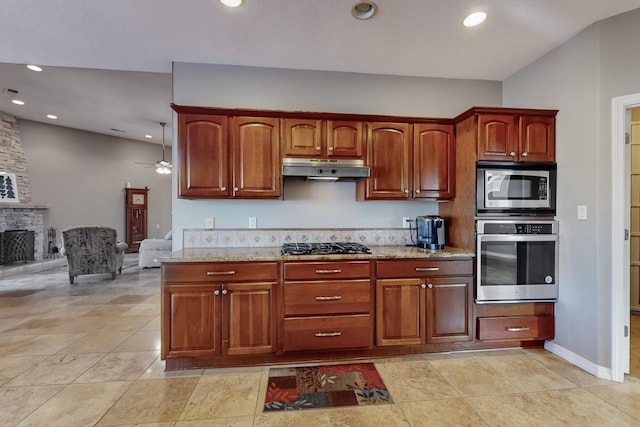 kitchen featuring ceiling fan, stainless steel appliances, a stone fireplace, and light stone countertops