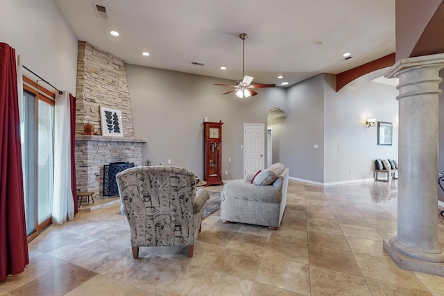 living room featuring ceiling fan, a towering ceiling, a stone fireplace, and decorative columns