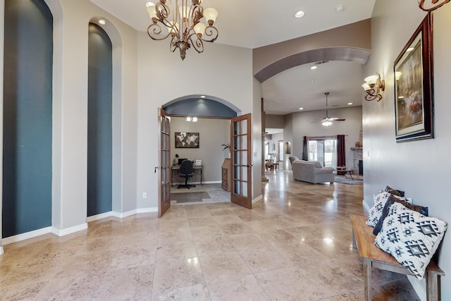 entryway with a fireplace, french doors, a towering ceiling, and ceiling fan with notable chandelier