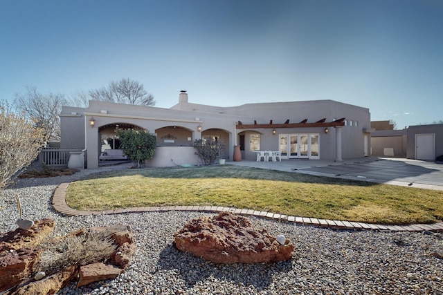 pueblo-style house featuring a front lawn, french doors, and a patio