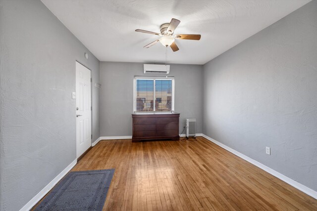 spare room featuring ceiling fan, a wall mounted AC, hardwood / wood-style floors, and radiator heating unit