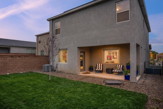 back of house at dusk with a patio area, fence, a lawn, and stucco siding