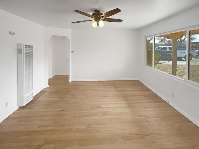 unfurnished room with arched walkways, light wood-style flooring, a heating unit, ceiling fan, and baseboards