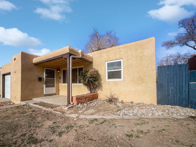 pueblo-style house featuring a patio area, an attached garage, fence, and stucco siding