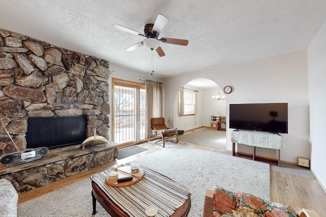 living room featuring a textured ceiling, ceiling fan, a fireplace, and light hardwood / wood-style flooring