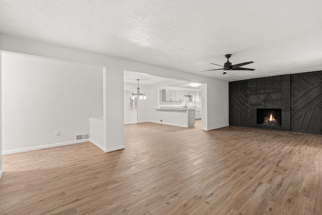 unfurnished living room featuring a textured ceiling, ceiling fan with notable chandelier, a fireplace, and light wood-type flooring