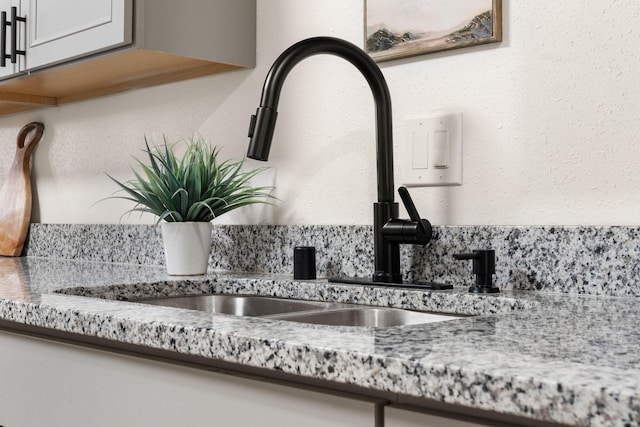 interior details with light stone counters, sink, and white cabinets