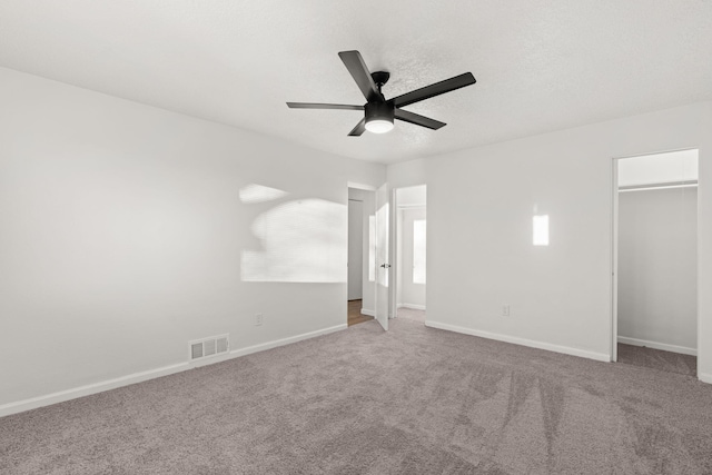 unfurnished bedroom with ceiling fan, a walk in closet, a textured ceiling, and carpet