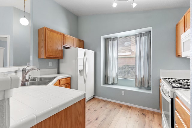 kitchen featuring white appliances, lofted ceiling, pendant lighting, light hardwood / wood-style flooring, and sink