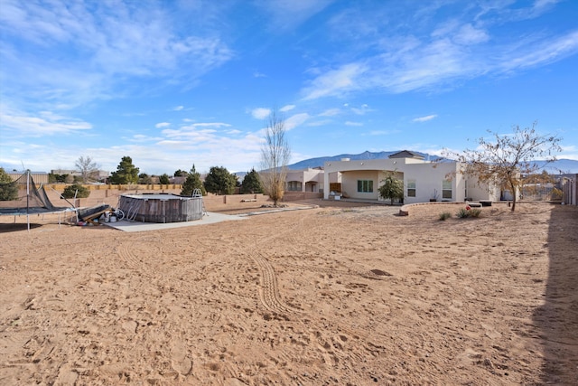 rear view of house with a trampoline, stucco siding, a jacuzzi, and fence