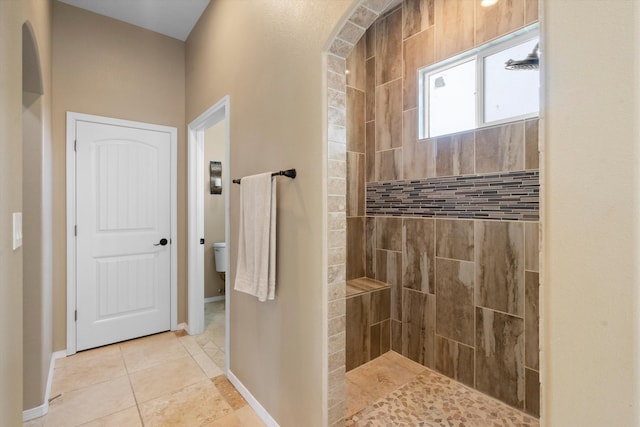 bathroom featuring toilet, tiled shower, and tile patterned flooring