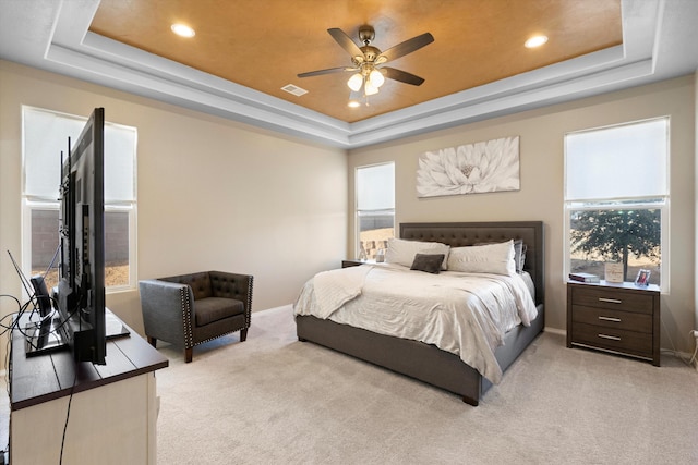 bedroom with a raised ceiling, light colored carpet, ceiling fan, and multiple windows