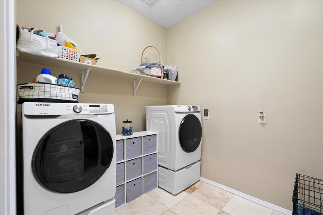 clothes washing area featuring washer and dryer, a textured ceiling, and light tile patterned flooring