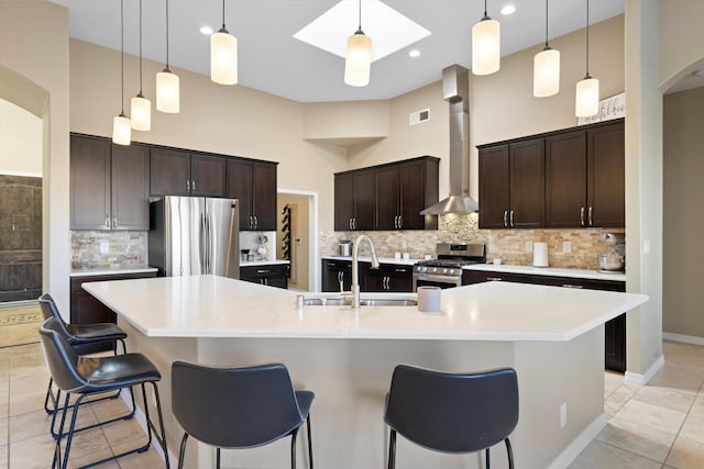 kitchen featuring visible vents, a high ceiling, appliances with stainless steel finishes, a sink, and wall chimney range hood