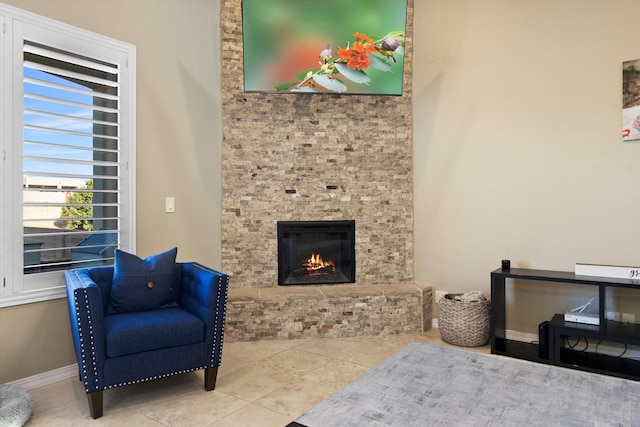 living area featuring tile patterned flooring, a stone fireplace, and baseboards