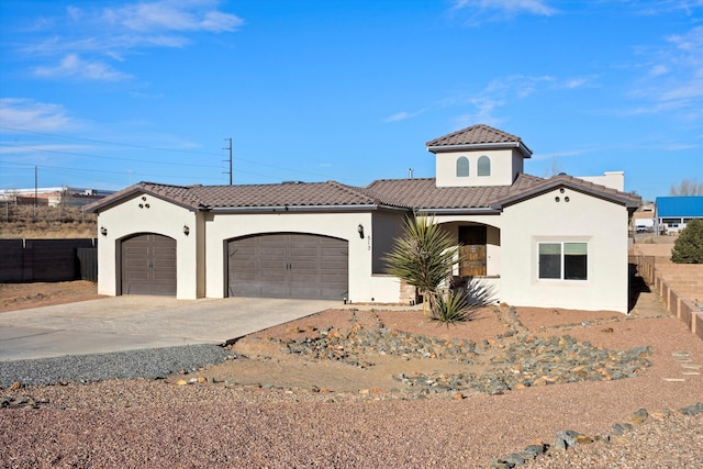 mediterranean / spanish-style house featuring a tile roof, stucco siding, concrete driveway, an attached garage, and fence