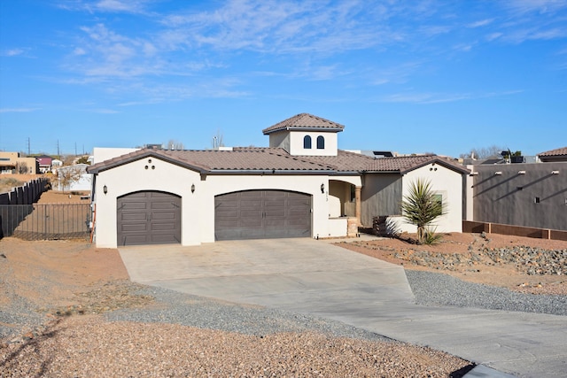 mediterranean / spanish house with stucco siding, an attached garage, fence, driveway, and a tiled roof