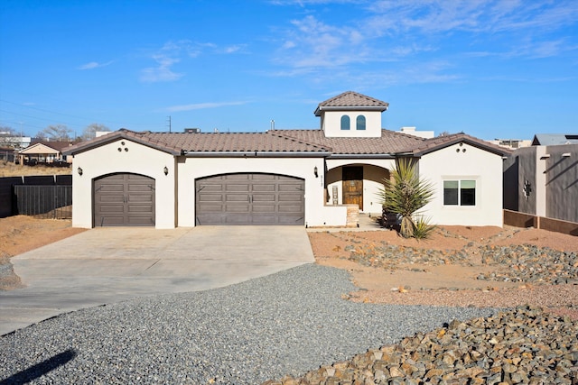 mediterranean / spanish home with fence, a tiled roof, an attached garage, and stucco siding