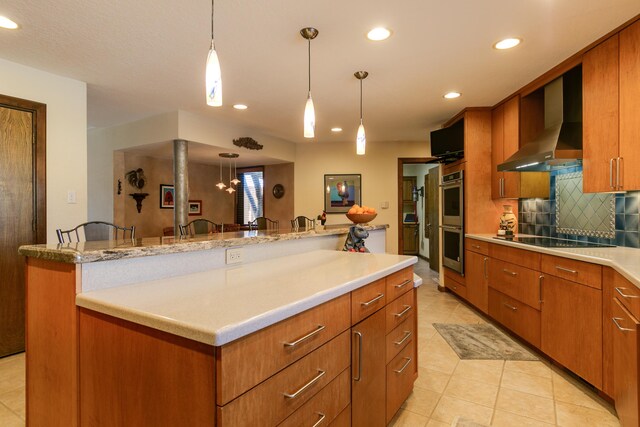 kitchen with pendant lighting, wall chimney range hood, a breakfast bar, black electric cooktop, and stainless steel double oven