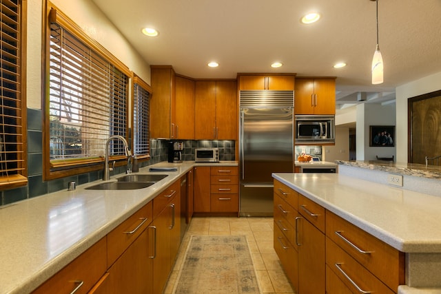 kitchen featuring sink, built in appliances, hanging light fixtures, light tile patterned floors, and backsplash