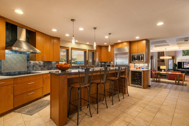 kitchen featuring pendant lighting, built in appliances, wine cooler, tasteful backsplash, and wall chimney exhaust hood