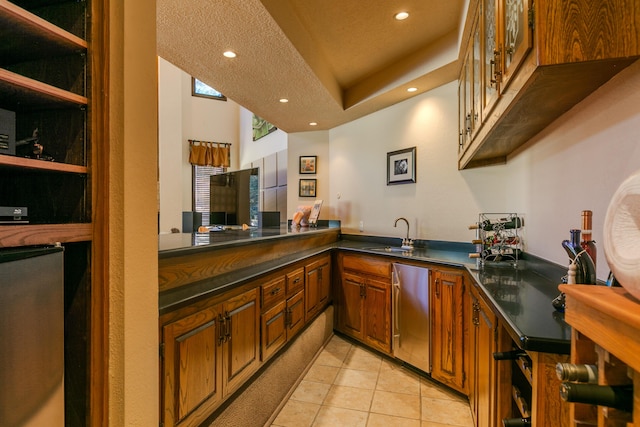 kitchen with sink, light tile patterned floors, stainless steel dishwasher, a tray ceiling, and kitchen peninsula