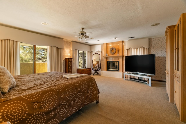 bedroom featuring a tiled fireplace, access to outside, ceiling fan, light carpet, and a textured ceiling