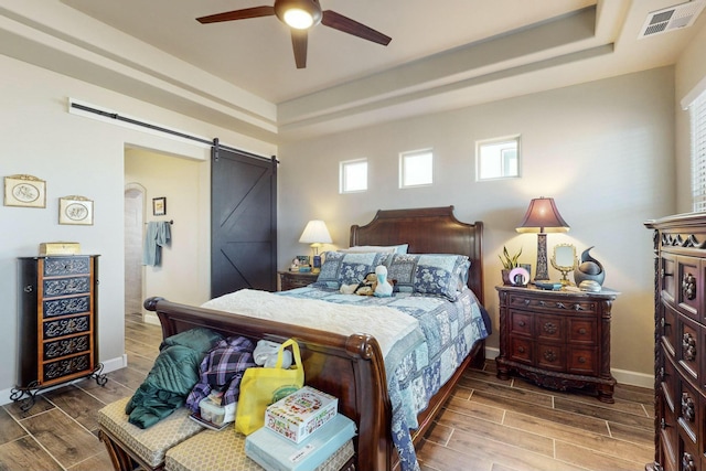 bedroom featuring ceiling fan, a raised ceiling, and a barn door