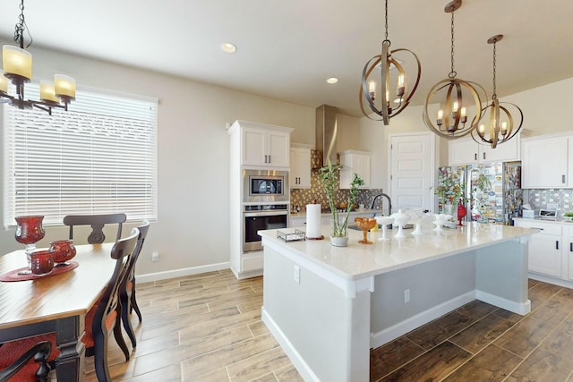 kitchen featuring decorative light fixtures, a center island with sink, decorative backsplash, stainless steel appliances, and white cabinets