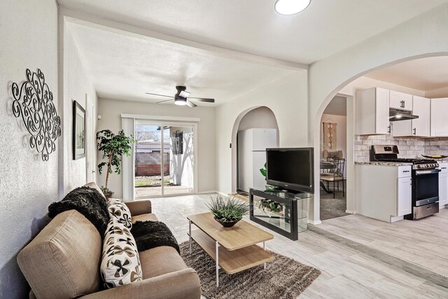 living room with ceiling fan, beam ceiling, and light wood-type flooring