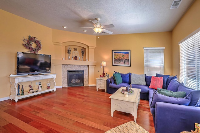 living area with visible vents, a textured ceiling, a glass covered fireplace, and wood finished floors