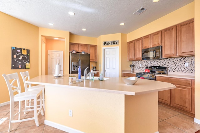 kitchen featuring a center island with sink, visible vents, light tile patterned flooring, stainless steel appliances, and backsplash