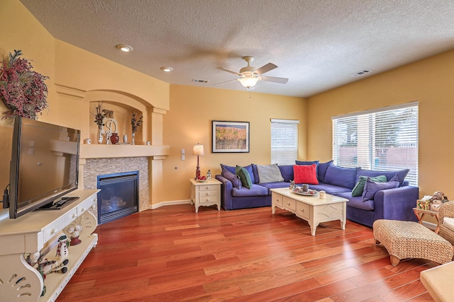 living area with a glass covered fireplace, wood finished floors, visible vents, and ceiling fan