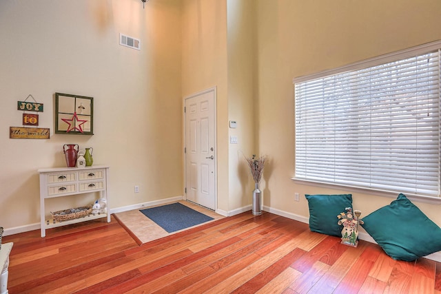 entryway with a high ceiling, wood finished floors, visible vents, and baseboards