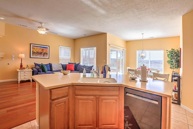 kitchen with an island with sink, a sink, stainless steel dishwasher, open floor plan, and light countertops