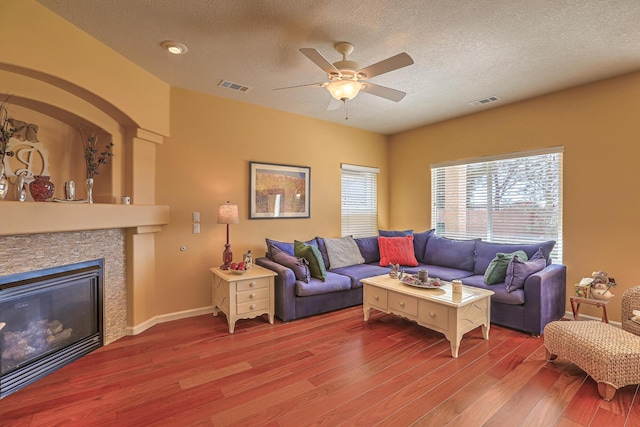 living area featuring a stone fireplace, visible vents, light wood finished floors, and ceiling fan