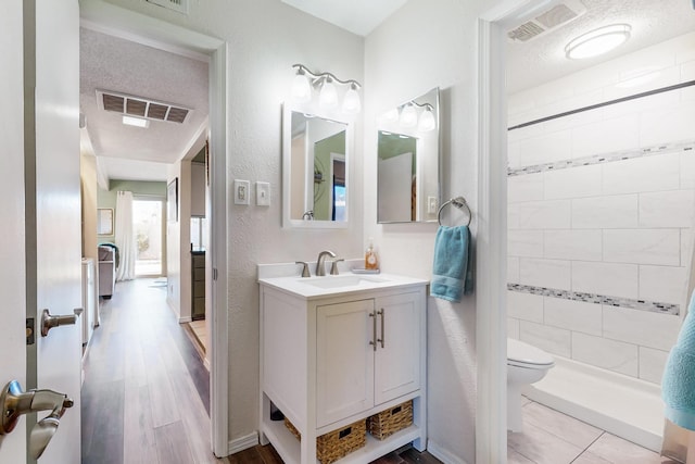 bathroom with toilet, vanity, hardwood / wood-style flooring, a textured ceiling, and a tile shower