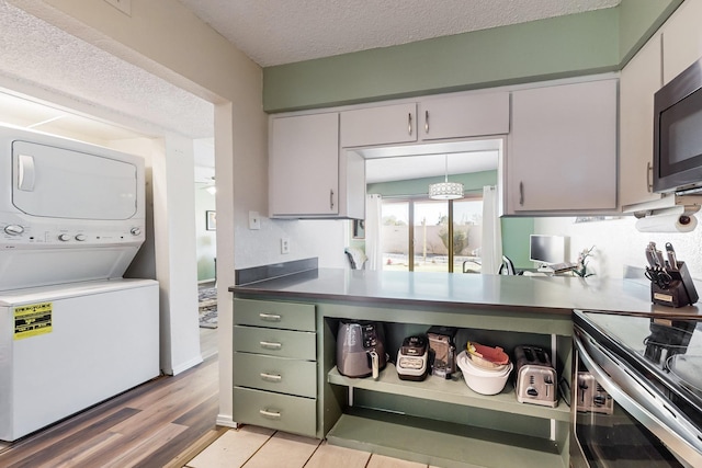 kitchen featuring light hardwood / wood-style floors, stacked washing maching and dryer, stainless steel electric range oven, a textured ceiling, and white cabinets