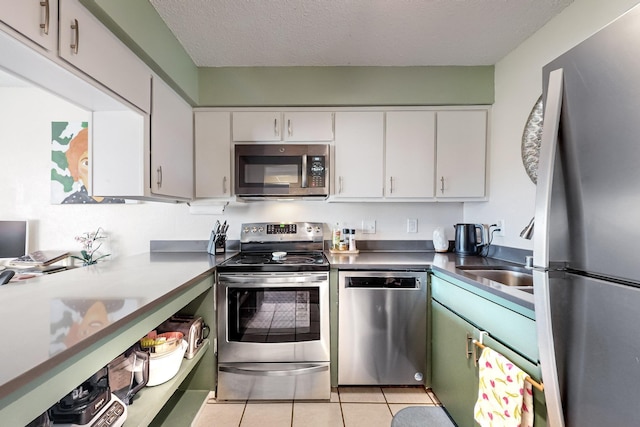 kitchen with sink, light tile patterned floors, appliances with stainless steel finishes, a textured ceiling, and white cabinets