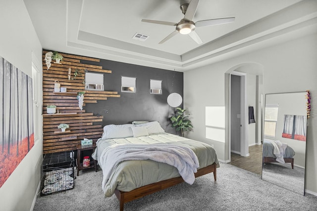 carpeted bedroom featuring ceiling fan and a raised ceiling