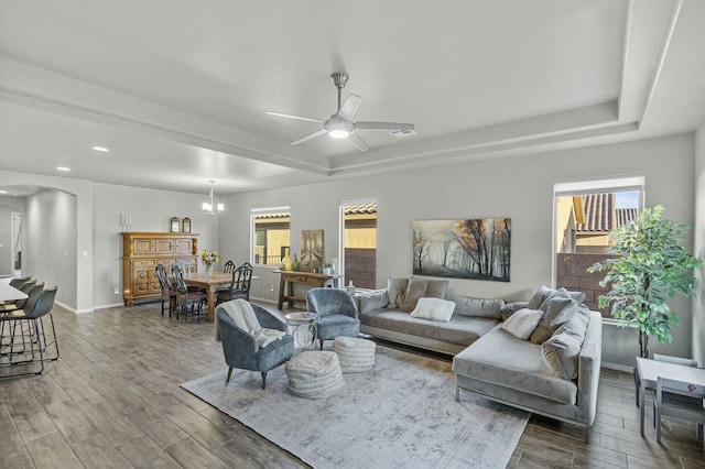 living area featuring arched walkways, ceiling fan with notable chandelier, a raised ceiling, and wood finished floors