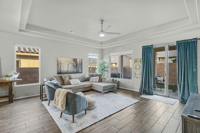 living room featuring visible vents, a ceiling fan, a tray ceiling, wood finished floors, and baseboards