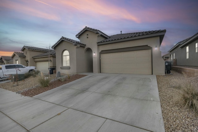 mediterranean / spanish-style home featuring a tile roof, stucco siding, an attached garage, and concrete driveway