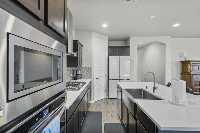 kitchen featuring a sink, stainless steel appliances, a center island with sink, and light countertops