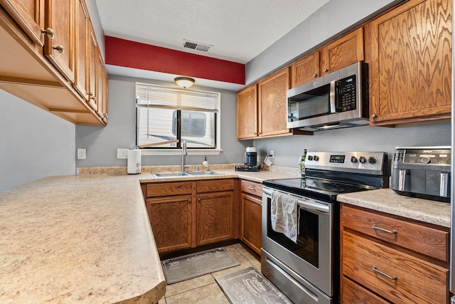 kitchen with a textured ceiling, appliances with stainless steel finishes, light tile patterned flooring, and sink