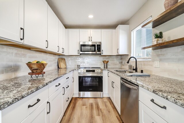 kitchen featuring white cabinetry, appliances with stainless steel finishes, backsplash, light wood-type flooring, and sink