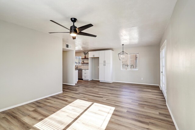 unfurnished living room with ceiling fan with notable chandelier, sink, and light hardwood / wood-style flooring