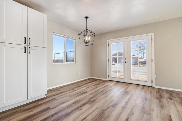 unfurnished dining area with light hardwood / wood-style floors, an inviting chandelier, french doors, and a healthy amount of sunlight