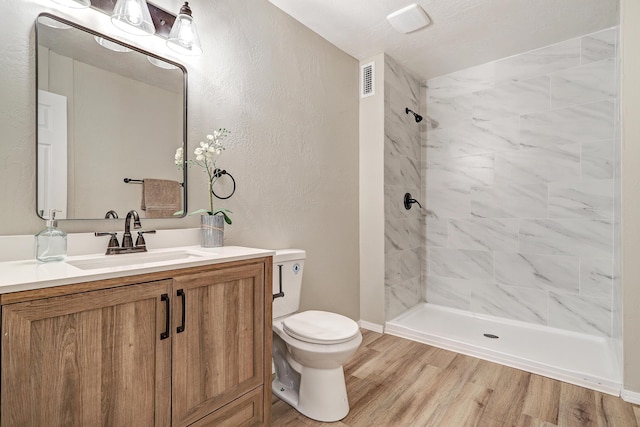 bathroom with toilet, vanity, tiled shower, and hardwood / wood-style floors