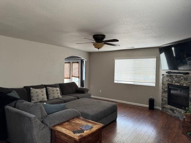 living room with dark hardwood / wood-style flooring, ceiling fan, a stone fireplace, and a textured ceiling